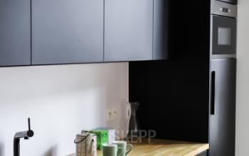 Moderne pantry ruimte met zwarte kasten en een houten werkblad, voorzien van een gootsteen en ingebouwde apparaten, in het kantoor te huur op Rue du Congres 37, Brussel.