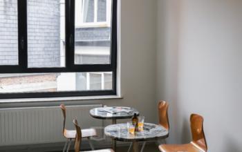 Vergaderruimte te huur op Rue du Congres 37, Brussel, met ronde tafels, houten stoelen en veel natuurlijk licht.