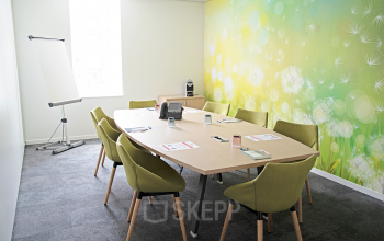 Bright conference room at Louizalaan / Avenue Louise 143 in Brussels Elsene, featuring a large meeting table, green chairs, and a vibrant wall mural.