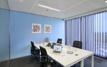 Modern kantoor te huur op Louizalaan in Brussel Elsene, voorzien van een vergaderruimte met glazen wand, drie bureaustoelen, wit bureau en kleurrijke kunstwerken aan de muur.