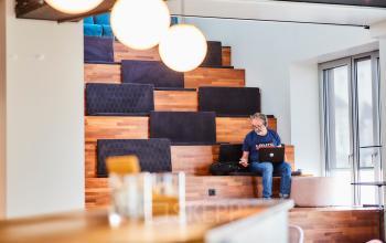 Man met laptop in informele vergaderruimte met houten zitplaatsen, kantoorpand Louizalaan / Avenue Louise 54, Brussel Elsene.