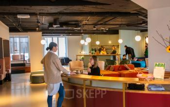 Een sfeervolle kantoorruimte te huur op Louizalaan / Avenue Louise 54 in Brussel Elsene, met moderne meubels, lounge en werkplekken. Mensen overleggen aan de balie en werken aan tafels.