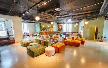 Moderne kantoorruimte te huur Louizalaan 54 in Brussel Elsene, met kleurrijke zitbanken, ruime vergadertafels en een bar met stoelen.