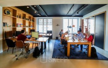 Kantoor te huur aan de Louizalaan 54 in Brussel Elsene, moderne kantoorruimte met grote ramen en houten meubels, mensen aan het werk achter computers.