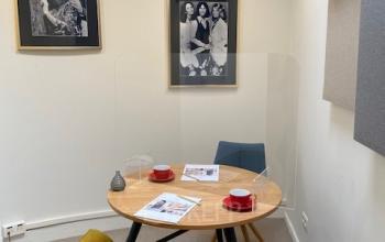 Compact furnished office space with a round wooden table, yellow chair, two framed photos on the wall, and a lamp at Louizalaan / Avenue Louise 367, Brussels Elsene.