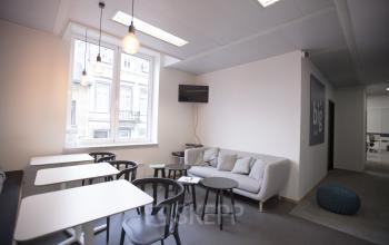 Modern office lounge area at Avenue Louise 367, Brussels Elsene, featuring tables, chairs, a comfortable sofa, and a flat-screen TV, ideal for office space rental.