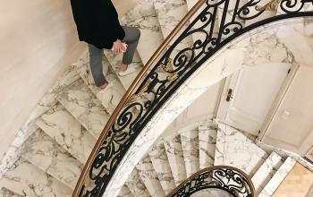 Elegant spiral staircase with marble steps and ornate railing, featuring a woman walking upwards in a Brussels office space.