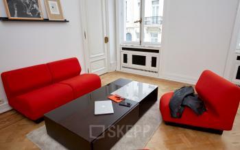Modern office space at Louizalaan / Avenue Louise 367 in Brussels Elsene with red sofas, a dark coffee table, and a laptop.