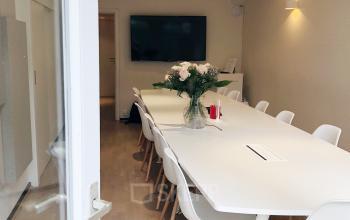 Vergaderruimte in kantoorruimte te huur op Priester Cuypersstraat / Rue Abbé Cuypers 3 in Brussel Etterbeek, voorzien van een lange witte tafel, stoelen, bloemen en een flatscreen.