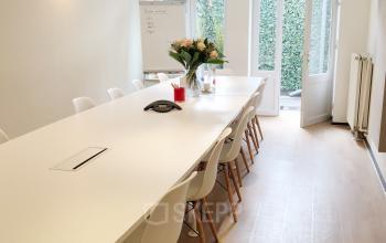 Moderne vergaderruimte te huur in Brussel Etterbeek, gelegen op Priester Cuypersstraat / Rue Abbé Cuypers 3, met lange witte tafel en stoelen, voorzien van bloemen en een schrijfblok.