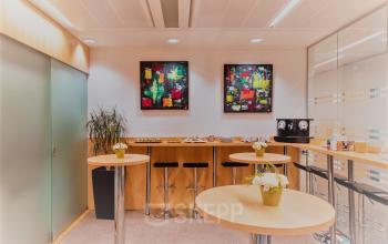 Foto van een gemeubileerde kantoorruimte te huur in Meeûssquare / Square de Meeûs 38-40, Europese Wijk, Brussel. De ruimte heeft hoge tafels en schilderijen aan de wand.