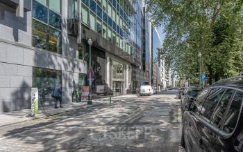 Exterior of office buildings at Meeûssquare / Square de Meeûs 37 in Brussels European District, showing a street view with cars parked along the curb and a few pedestrians.