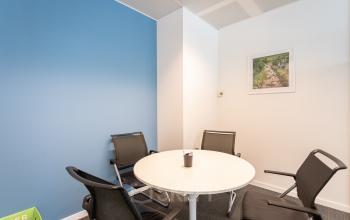 Small office meeting room with a round white table, surrounded by four black chairs, located at Meeûssquare/Square de Meeûs 37 in Brussels European District.