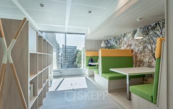 Modern office space rental with green and yellow seating booths, natural light, and wooden furnishings at Meeûssquare / Square de Meeûs 37, Brussels European District.