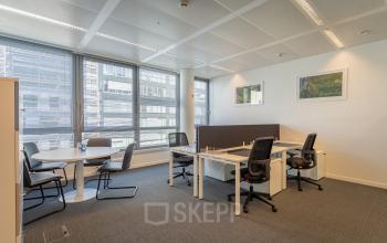 Modern office space rental with large windows, workstations, and a small round meeting table, located at Meeûssquare / Square de Meeûs 37 in Brussels European District.