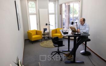 Kantoorruimte te huur op Avenue Palmerston 3, in de Europese Wijk, Brussel. Man aan het werk op laptop in een modern ingerichte kantoorruimte met gele stoelen en bureau.