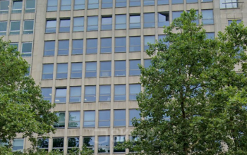 Exterieur van kantoorgebouw op Avenue des Arts 3-5, Brussel Europese Wijk, met moderne glazen gevel en omliggende groene bomen; kantoorruimte te huur beschikbaar.