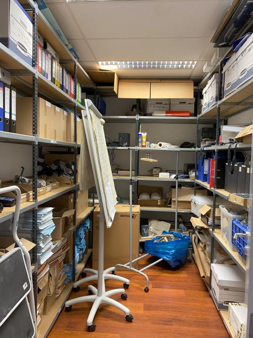 Interior storage area in Avenue des Arts 3-5, Brussels European District, filled with shelves, office supplies, and a whiteboard. Ideal for office space rental needing ample storage options.