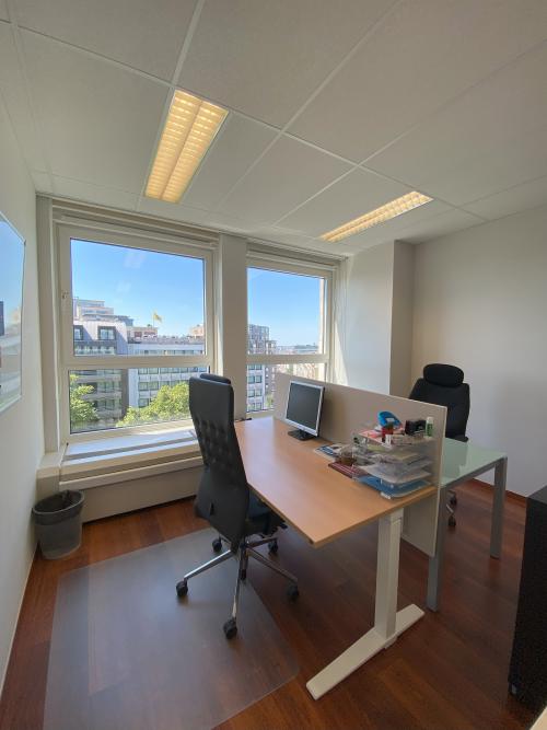 Bright office to rent at Avenue des Arts 3-5, Brussels European District, featuring a desk with chairs and a city view through large windows.