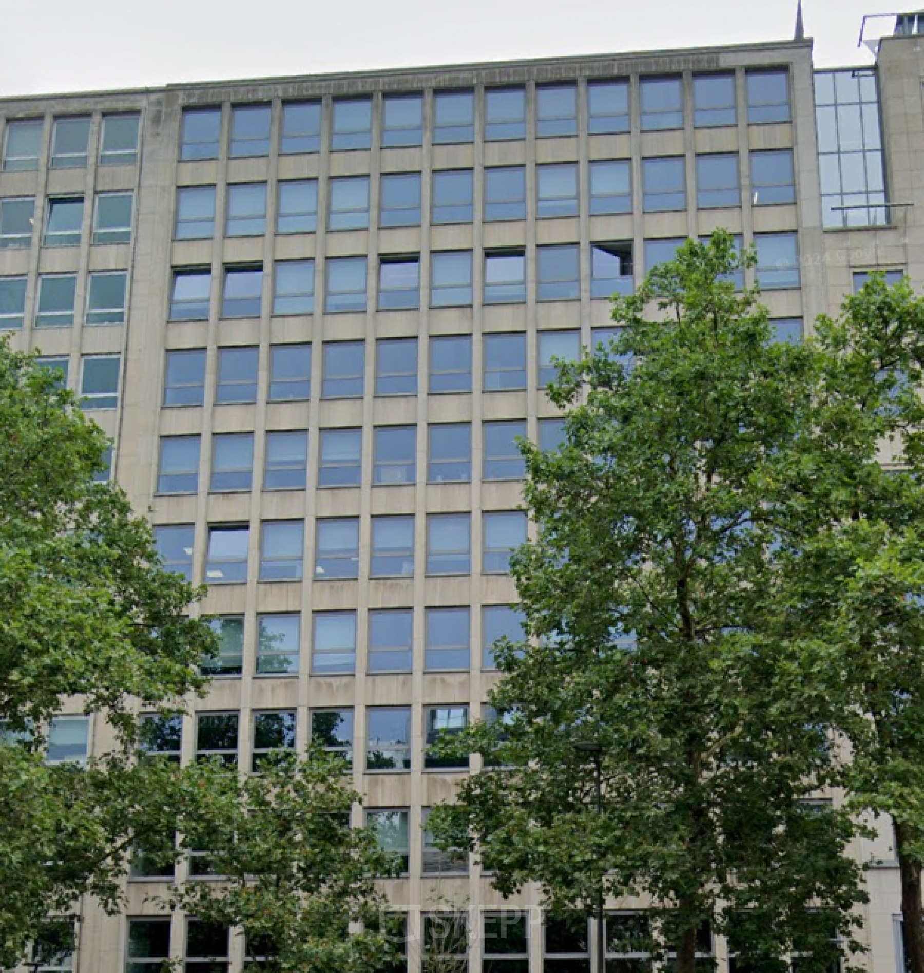 Exterieur van kantoorgebouw op Avenue des Arts 3-5, Brussel Europese Wijk, met moderne glazen gevel en omliggende groene bomen; kantoorruimte te huur beschikbaar.