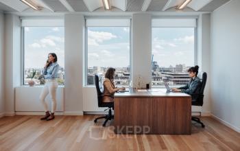 Spacious office to rent in Brussels European District with two employees working at desks and one person on the phone by the window.
