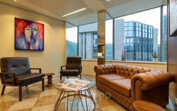 Cozy furnished lounge area with modern chairs and a leather sofa, large window view of Brussels European District at Robert Schumanplein 2-4, ideal for office space rental.