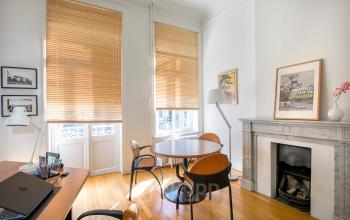 Kantoorruimte te huur in Brussel Europese Wijk, Breydelstraat / Rue Breydel 34-36, lichte kamer met houten vloeren, grote ramen met jaloezieën, ronde tafel met stoelen, bureau, en decoratieve open haard.