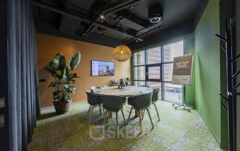 Bright office space at Rietbaan 40-42 in Capelle aan den IJssel, featuring a modern conference room with a round table, chairs, large plant, and wall screen. Ideal for office space rental.