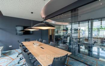 Modern conference room with a large wooden table and ergonomic chairs, featuring sleek lighting and a wall-mounted screen, perfect for office space rental at Rhijnspoor 209-263, Capelle aan den IJssel.