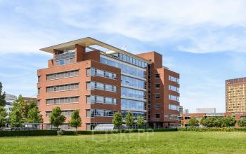Exterior view of the modern red-brick office building located at Fascinatio Boulevard 522, Capelle aan den IJssel, ideal for office space rental. The building is surrounded by lush greenery.