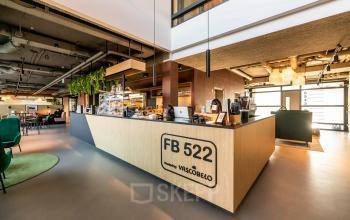 Modern interior of office space at Fascinatio Boulevard 522, featuring a stylish reception with greenery, wooden accents, and a cozy coffee bar, perfect for office space rental. Bright and inviting atmosphere for business needs.
