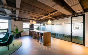 Modern office space with a large table and high chairs, surrounded by natural light from large windows, suitable for team collaboration at Fascinatio Boulevard 522, Capelle aan den IJssel. Office space rental available.