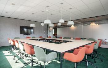 Modern conference room at Fascinatio Boulevard 522, Capelle aan den IJssel, featuring a large square table with colorful chairs and overhead lighting, ideal for professional meetings. Office space rental available.