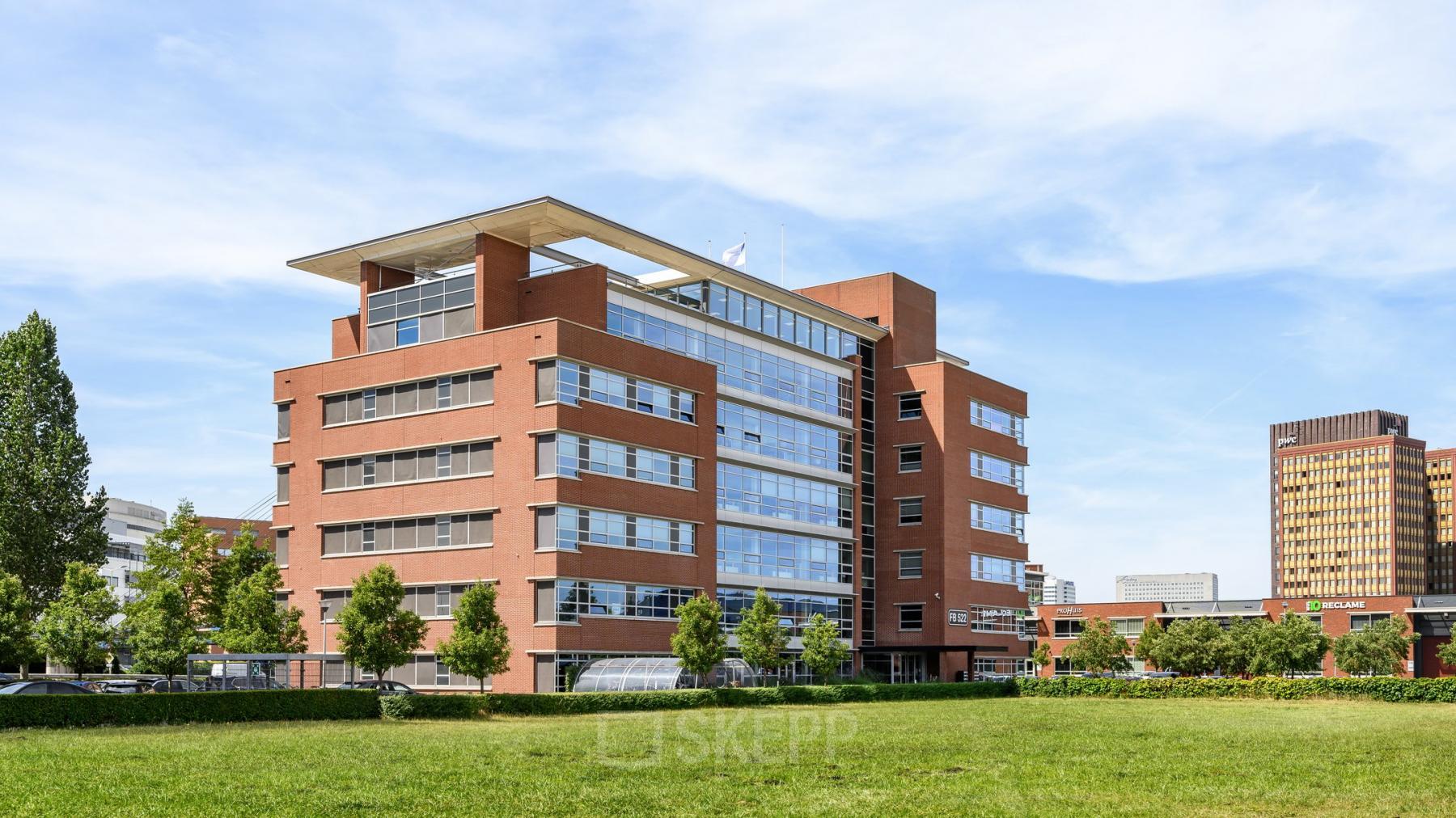 Exterior view of the modern red-brick office building located at Fascinatio Boulevard 522, Capelle aan den IJssel, ideal for office space rental. The building is surrounded by lush greenery.