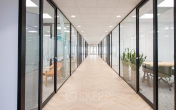 Spacious corridor inside Rivium Quadrant 75 office building in Capelle aan den IJssel, featuring glass-walled meeting rooms and modern furnishings, perfect for office space rental.