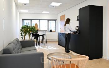 Modern office space rental at Rivium Quadrant 75, Capelle aan den IJssel, featuring a cozy lounge area, a stylish kitchenette, and a view of colleagues engrossed in work and coffee preparation.