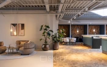 Modern office with stylish furnishings, featuring seating areas and plants, ideal for office space rental.