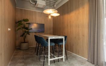 Furnished office space for rent at Essebaan 63, Capelle aan den IJssel, featuring a high table with chairs, wooden walls, and a screen for presentations.