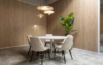 Cozy office space rental with round table, chairs, modern lighting, and a plant in a wood-paneled room at Essebaan 63.