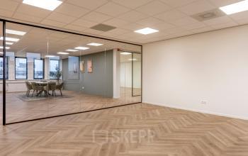 Open office space with hardwood floors and glass-walled conference room at Vlierbaan 20, ideal for office space rental in Capelle aan den IJssel.