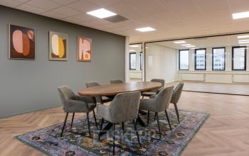 Furnished office space at Vlierbaan 20, Capelle aan den IJssel, showcasing a conference room with a wooden table, chairs, and wall art. Bright natural lighting enhances the atmosphere for office space rental.