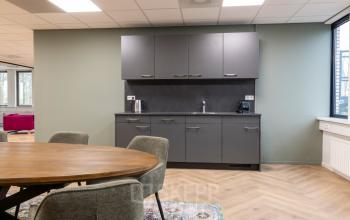 Modern furnished office space for rent at Vlierbaan 20 with a kitchenette featuring dark cabinets and a round table with chairs.