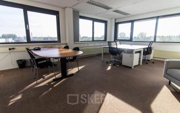 Bright office space for rent at Marshalllaan 2, Delft, featuring large windows, desks, and chairs suitable for a productive work environment.