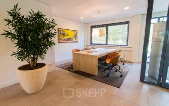 Bright office space at Marshalllaan 2, Delft, featuring a stylish meeting area with a large table, comfortable chairs, and a decorative plant. Perfect for anyone looking to rent office space.