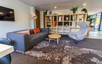 Cozy office space for rent at Marshalllaan 2, Delft, featuring a furnished lounge with a sofa, armchair, and decorative shelving. Ideal for office space rental.