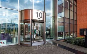 Exterior view of the office building at Olof Palmerstraat 10, Delft, featuring a glass entrance with a revolving door marked '10' and a modern design suitable for office space rental opportunities.