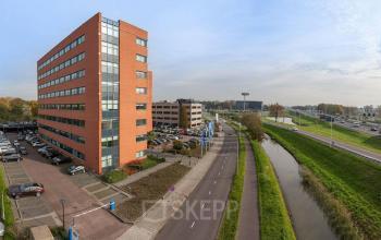 Exterior view of an office building at Olof Palmestraat 10, Delft, showcasing the available office space rental near a canal and highway.