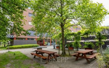 Exterior view of an office building at Delftechpark 9, Delft, featuring a green outdoor seating area ideal for office space rental breaks.