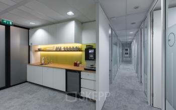 Modern office space rental at Willemsplein 2, Den Bosch featuring a sleek pantry with cabinets and a hallway leading to private offices.