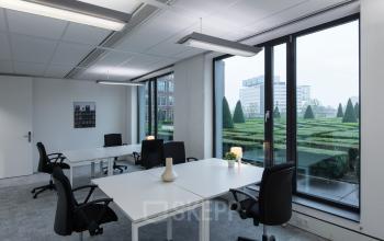 Modern office space to rent at Willemsplein 2 in Den Bosch with large windows, desks, and office chairs overlooking a well-maintained garden.
